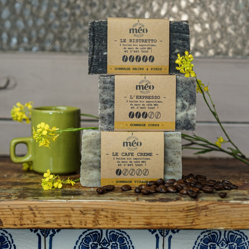 Savons exfoliants au marc de café MöBiUS (café crème, expresso, ristretto) empilés sur une tablette en bois avec fleurs de colza et grains de café