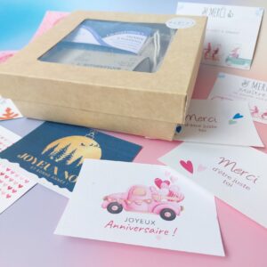 Coffret cadeau MöBiUS avec des cartes illustrées variées disposées tout autour : merci maître.sses, mamie chérie, joyeuses fêtes, et plus encore.