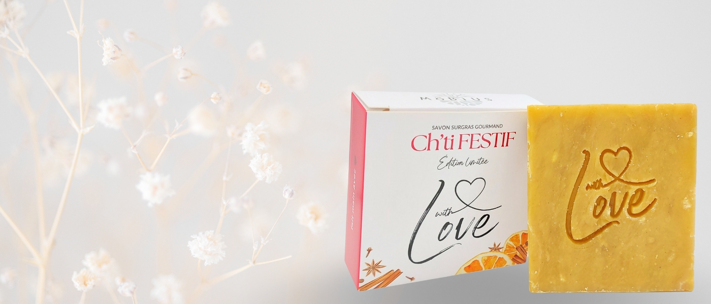 Bannière avec le savon Ch'ti Festif édition limitée "Love" sur fond gris, fleurs blanches nettes et floues à gauche, boîte et savon vrac à droite.