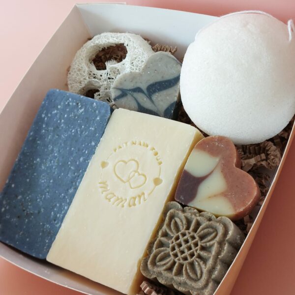 Coffret kraft à fenêtre carrée ouvert, contenant des savons et accessoires MöBiUS sur fond saumon.