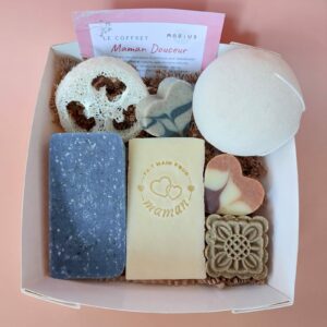 Coffret kraft à fenêtre carrée ouvert, contenant des savons et accessoires MöBiUS sur fond saumon.
