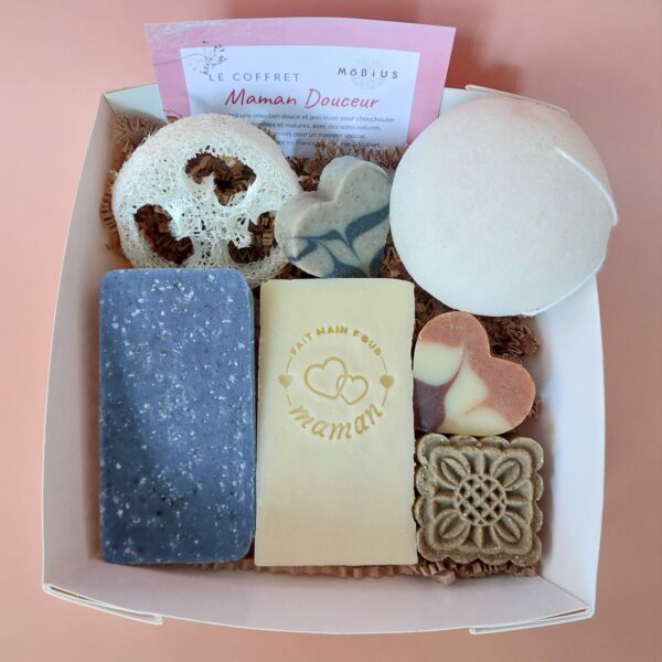 Coffret kraft à fenêtre carrée ouvert, contenant des savons et accessoires MöBiUS sur fond saumon.