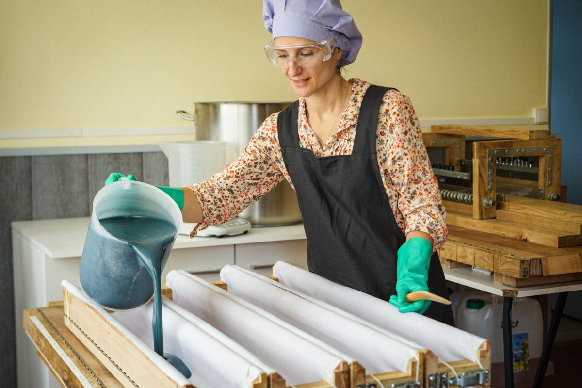 Virginie en tenue de laboratoire verse la pâte du savon saponifié à froid Lavande & Rhassouldans les moules, avec plusieurs moules au premier plan et casseroles en arrière-plan.