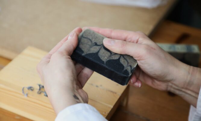 Virginie rabote à la main un savon Secret d’Alep MöBiUS, symbole du savoir-faire artisanal et du plaisir d’offrir du savon à Noël.