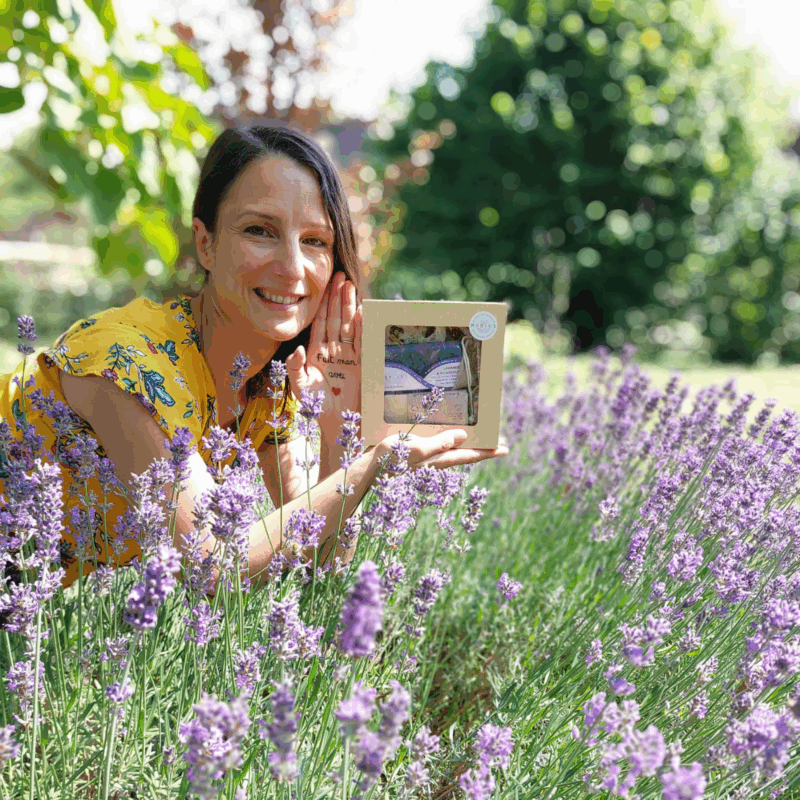 Virginie tenant un coffret cadeau MöBiUS avec savon lavande & rhassoul, au milieu d'un champ de lavande, avec la main tendue portant l'inscription "fait main avec ❤️" et arrière-plan naturel flou.