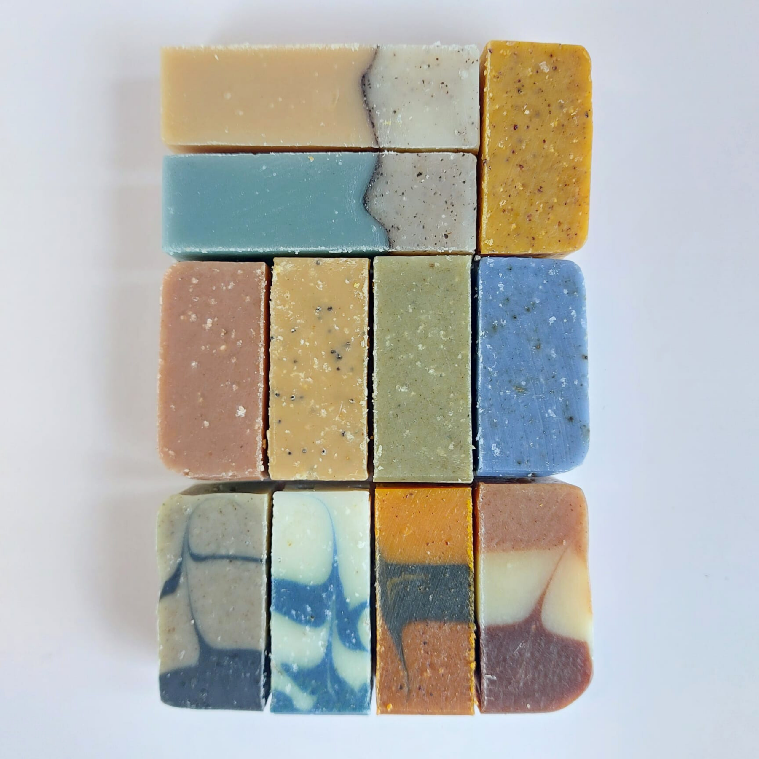 Onze mini-savons artisanaux MöBiUS saponifiés à froid, alignés sur fond blanc, montrant leurs couleurs et textures variées.