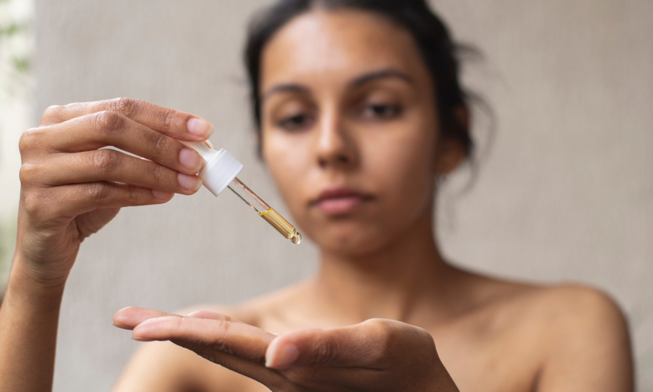 Femme appliquant quelques gouttes d'huile sur la main avec une pipette – routine skincare minimaliste