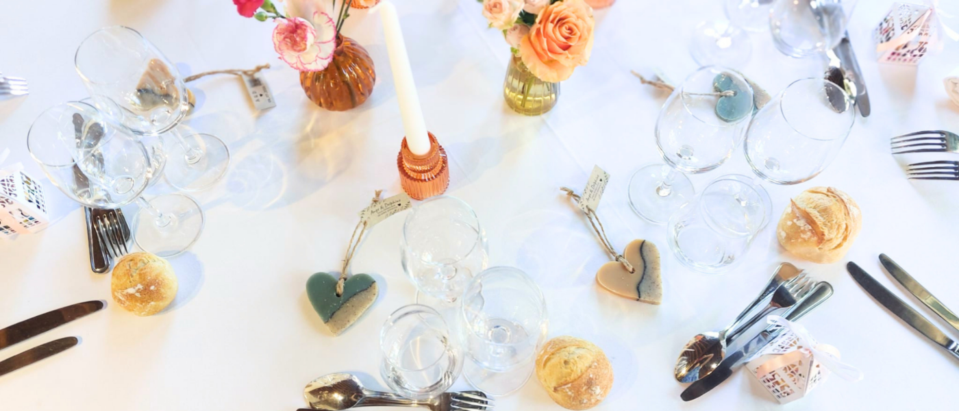 Table de mariage décorée avec des suspensions en savon artisanales en forme de cœur offertes comme cadeaux d'invités, entourées de fleurs, de bougies et de verres.